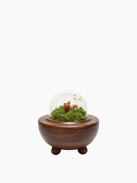 Håndlaget urne til kjæledyr i mørkt tre med en glasskuppel som inneholder et lite mose-landskap og en liten hundefigur.