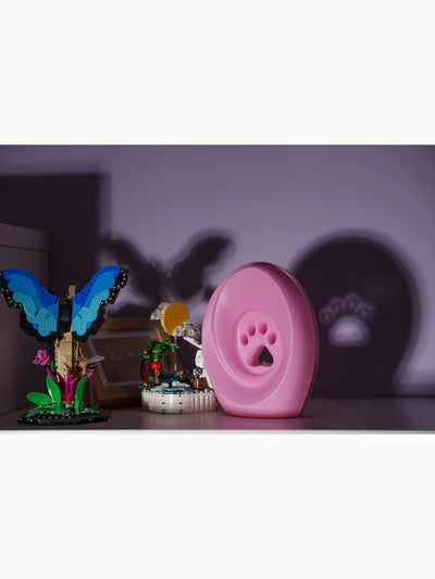 Rosa kjæledyrurne med poteavtrykk på hylle sammen med fargerike lekefigurer og sommerfuglskygge på veggen